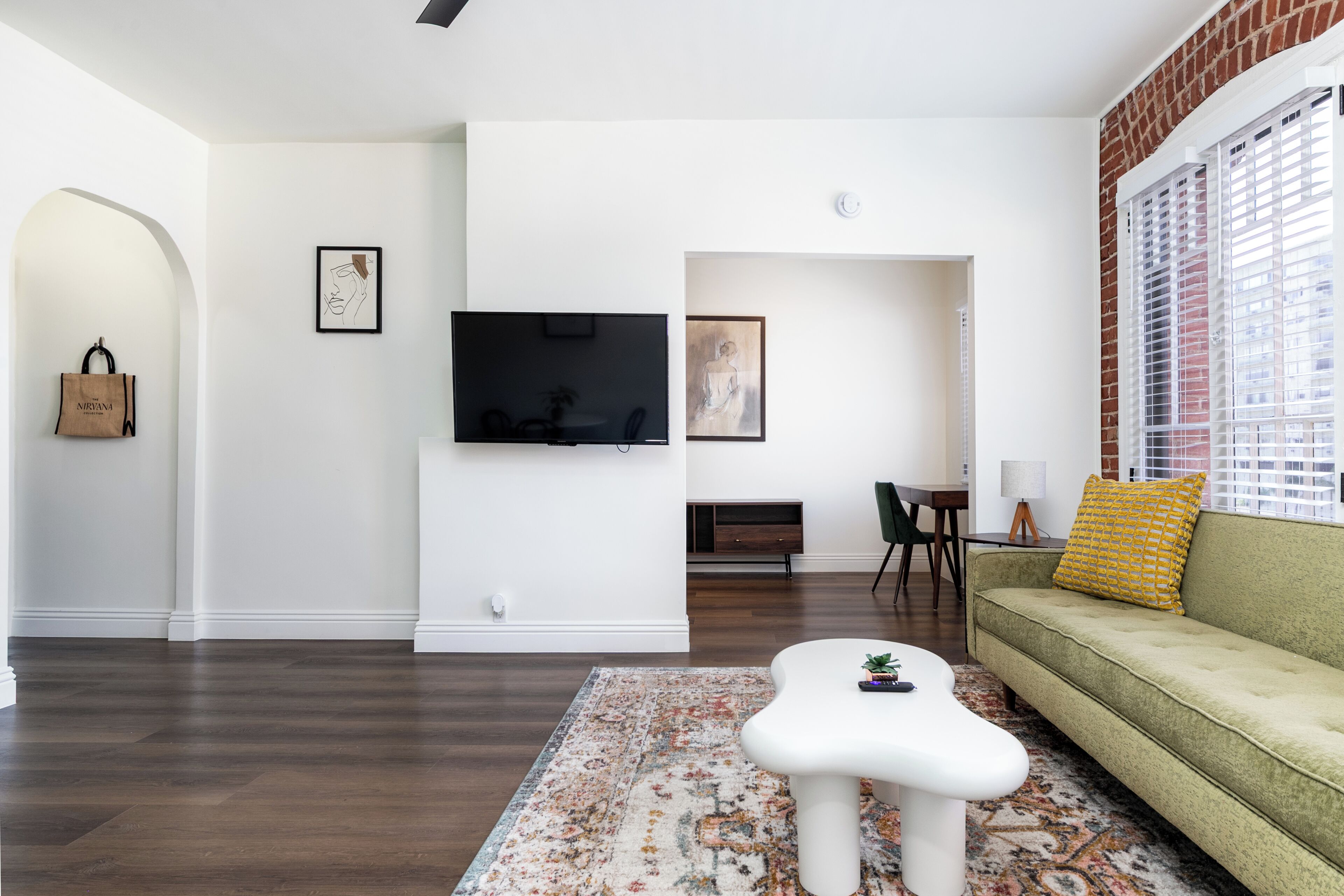 A modern living room with a flat-screen TV, a green sofa, a white coffee table, and a patterned rug.