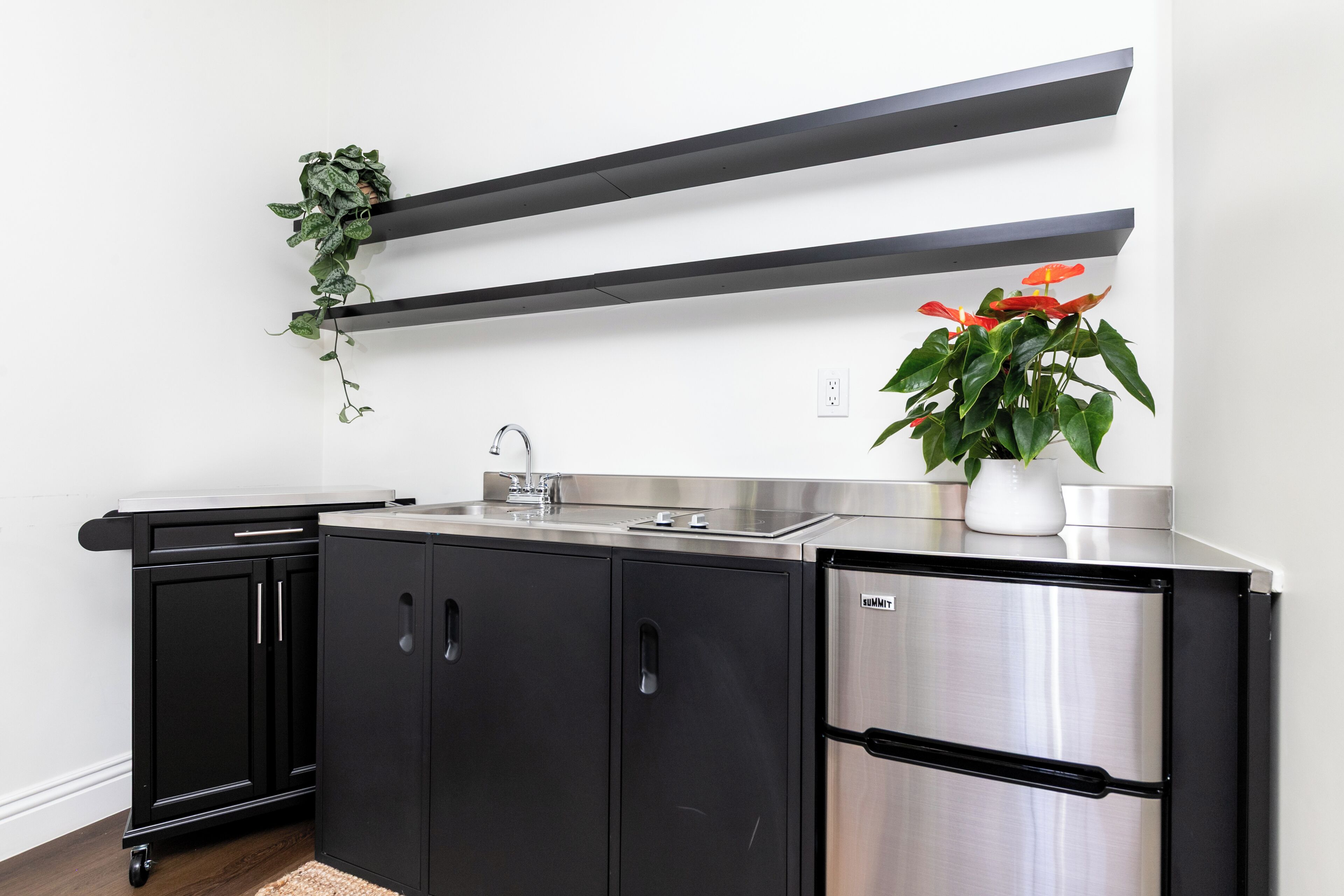 A modern kitchen with black cabinets, a stainless steel refrigerator, and two potted plants.