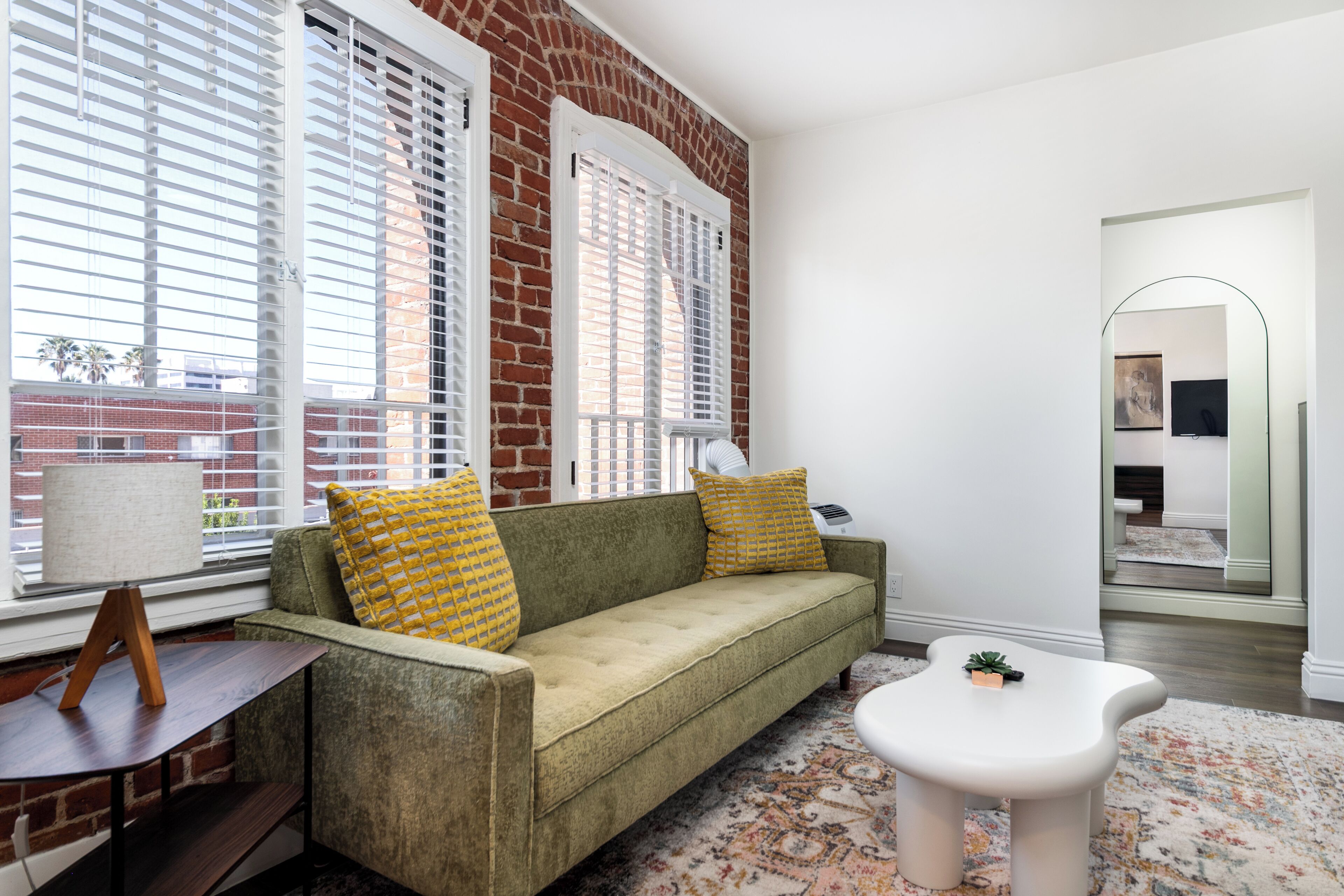A living room with a green sofa, yellow pillows, a white coffee table, and a patterned rug.