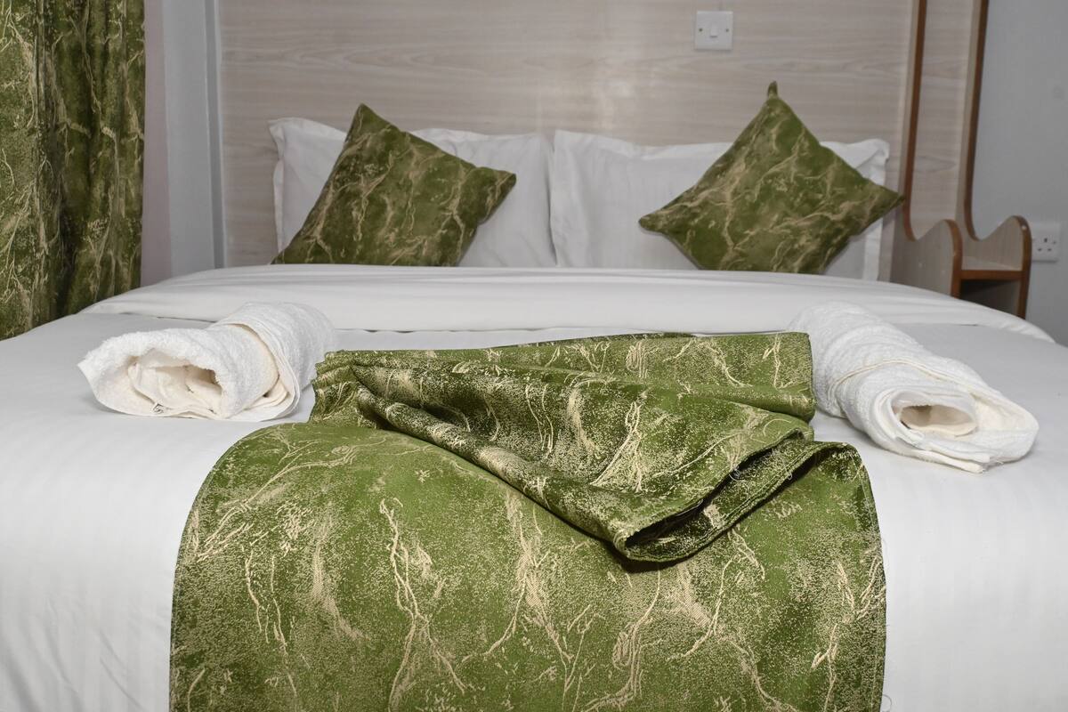 Ein ordentlich bezogenes Bett mit weißen Bettwäsche und einer grünen, gemusterten Decke.
