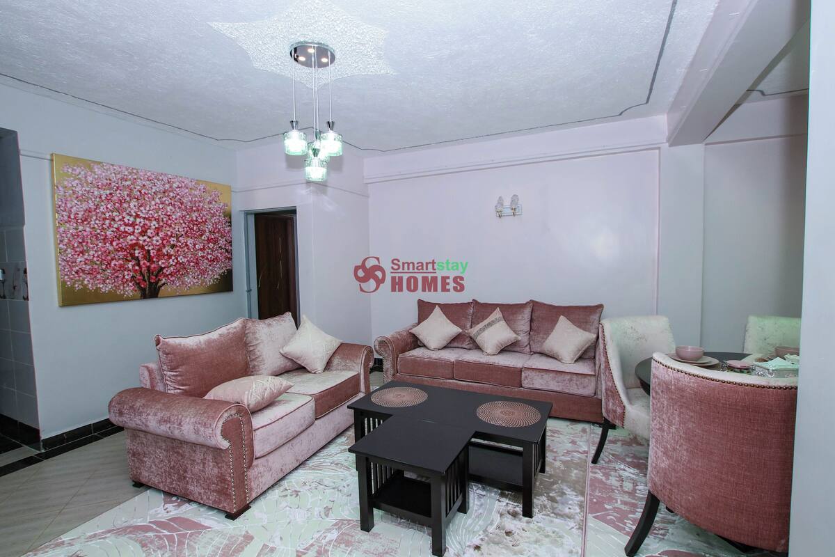 Ein Wohnzimmer mit zwei Sofas, einem Couchtisch und einem kleinen Tisch mit einer Schüssel. Ein Bild von rosa Blumen hängt an der Wand.