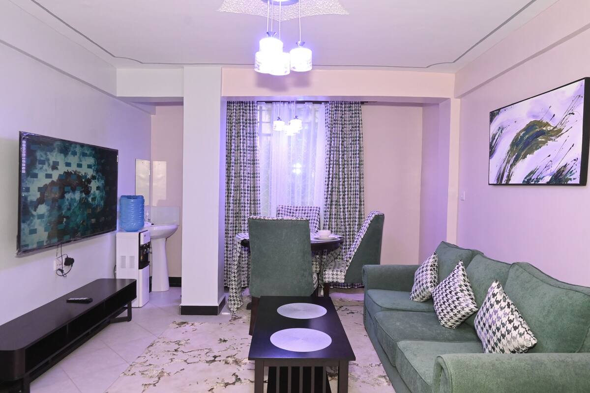 Ein modernes Wohnzimmer mit einem grünen Sofa, einem Esstisch und einem Fernseher.