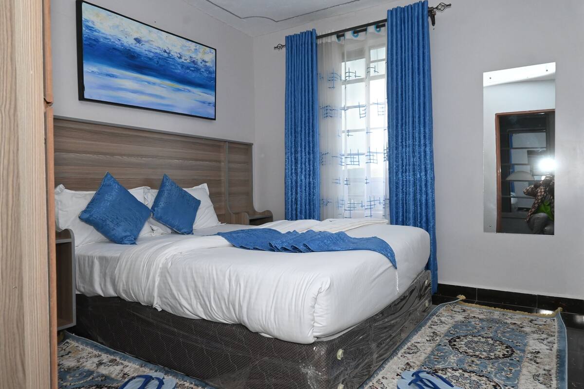 Ein ordentlich bezogenes Bett mit blauen Kissen, einer blauen Decke und einem gemusterten Teppich.