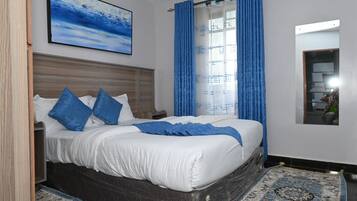A neatly made bed with blue pillows, a blue throw blanket, and a patterned rug on the floor.