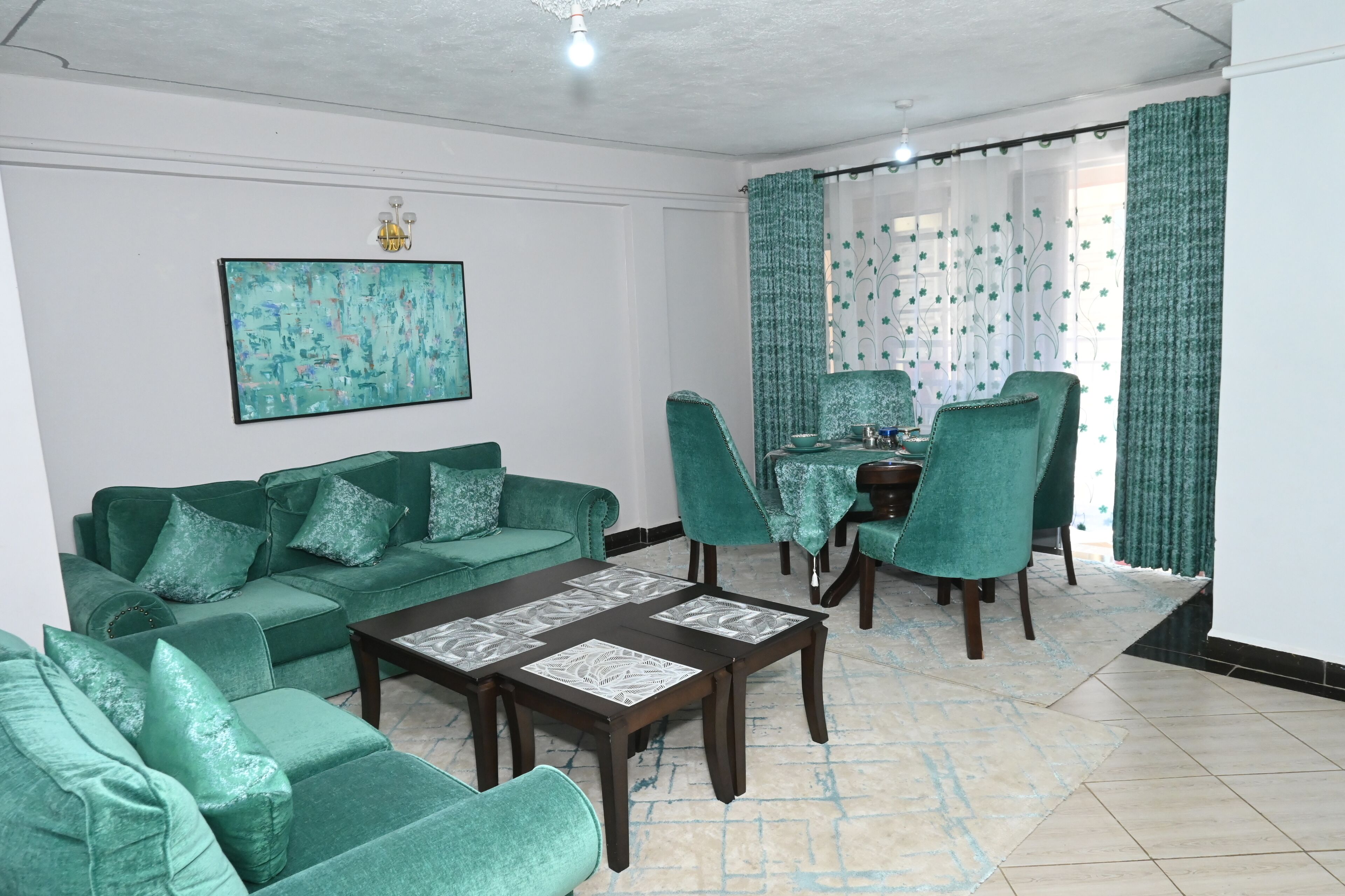 A living room with a green sofa set, a coffee table, and a dining area with a table and chairs.