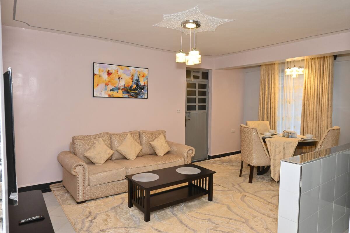 Ein Wohnzimmer mit einem beigefarbenen Sofa, einem dunkelholzigen Couchtisch, einem Esstisch mit Stühlen und einer Chandelier.
