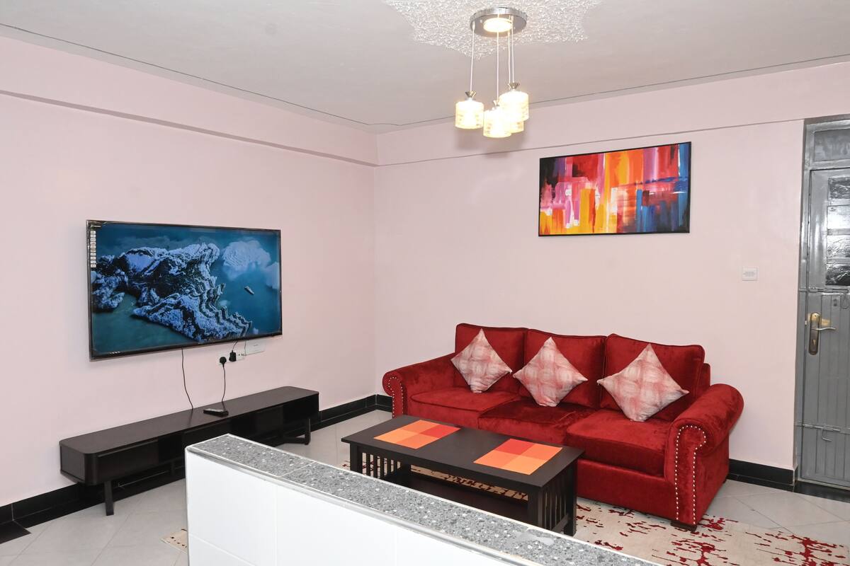 Ein modernes Wohnzimmer mit einem roten Sofa, einem Flachbildfernseher, einem Couchtisch und einem Gemälde an der Wand.