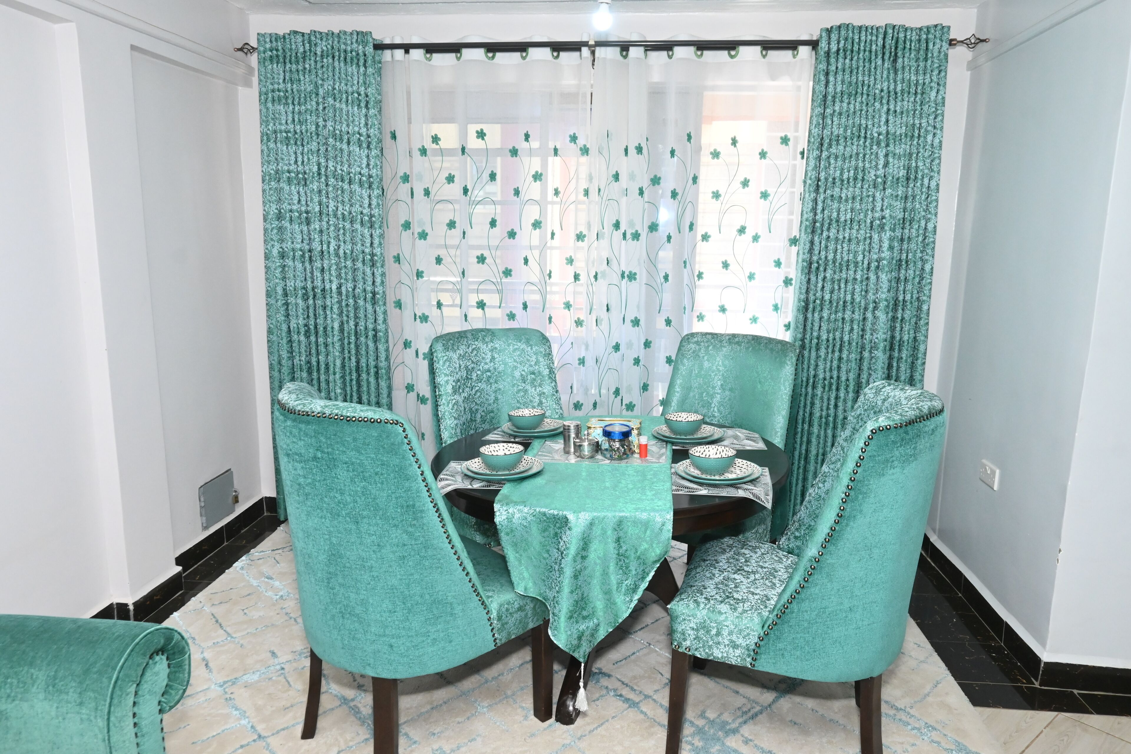 A dining area with a table set for four, surrounded by teal upholstered chairs.