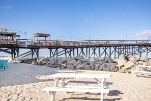 A pier extending over a sandy beach with a wooden structure, a rocky shoreline, and beach chairs. - "Paws. . . and RELAX!" A PF getaway in the clouds! (Carolina Beach)