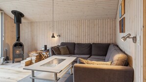 A cozy room with a wooden ceiling, a sofa, a table, and a fireplace. - Cozy summer house close to the beach (Grenå)