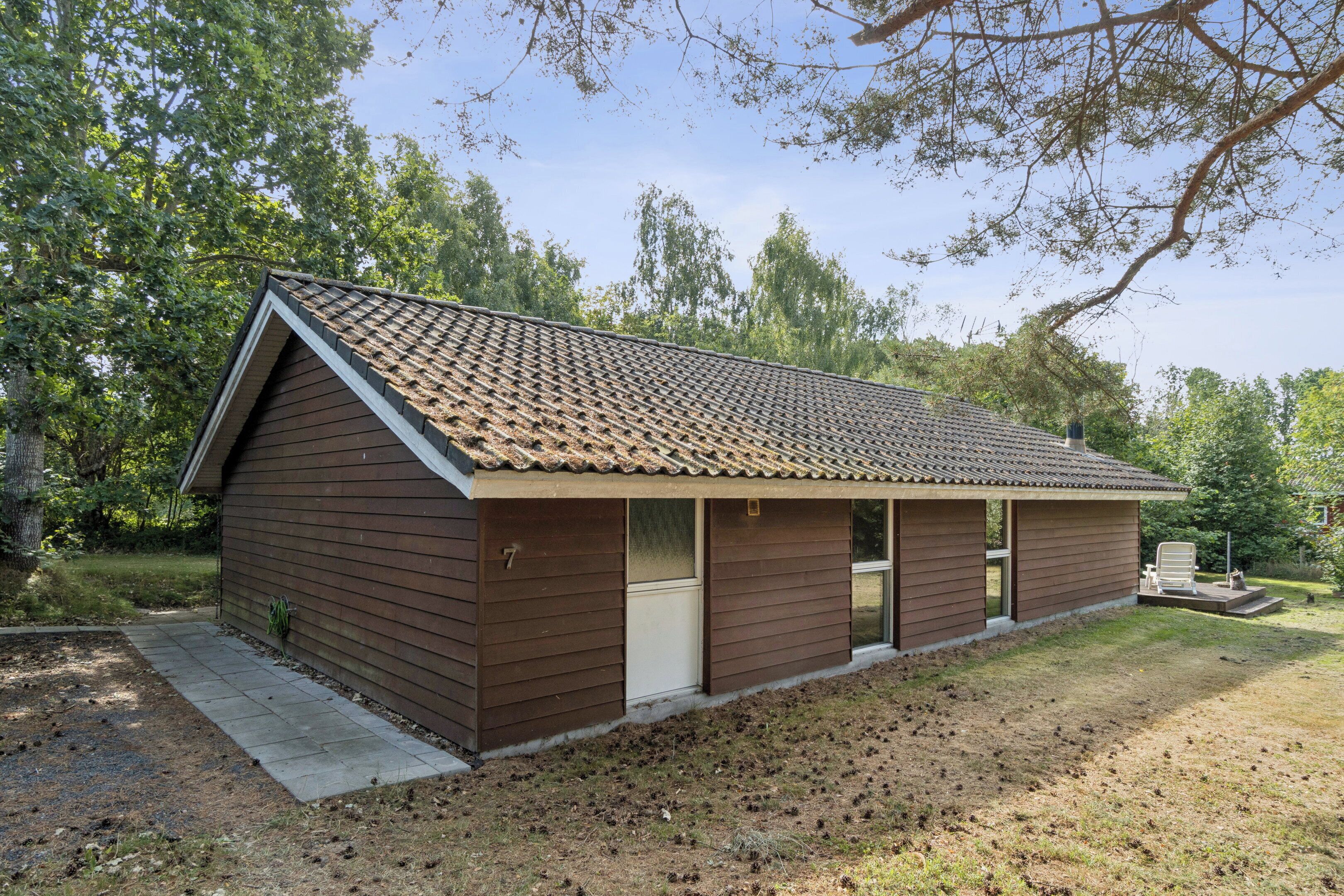 Une cabane de plain-pied avec un toit en pente, un porche à l’avant doté d’un banc et une petite terrasse.