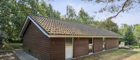 Une cabane de plain-pied avec un toit en pente, un porche à l’avant doté d’un banc et une petite terrasse.