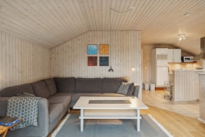 A cozy living room with a sectional sofa, a coffee table, and a kitchen area with cabinets and appliances. - Cozy summer house close to the beach (Grenå)