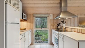A compact kitchen with wooden walls, a window, and a stainless steel range hood. - Cozy summer house close to the beach (Grenå)