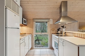 A compact kitchen with wooden walls, a window, and a stainless steel range hood.