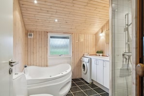 A bathroom with a bathtub, a washing machine, and a shower.