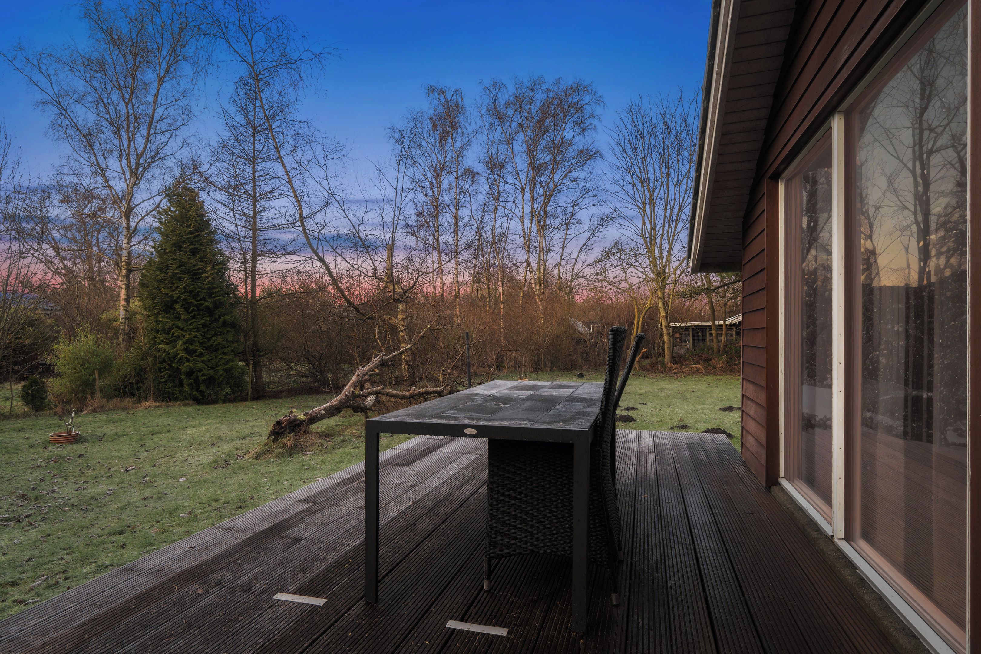 Une terrasse dotée d’une table et de chaises, entourée d’une autre terrasse en bois et offrant une vue sur les arbres et un paysage lointain.