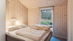 A wooden-paneled room with a bed, a window, and a wall-mounted light fixture. - Cozy summer house close to the beach (Grenå)