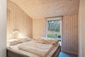A wooden-paneled room with a bed, a window, and a wall-mounted light fixture.