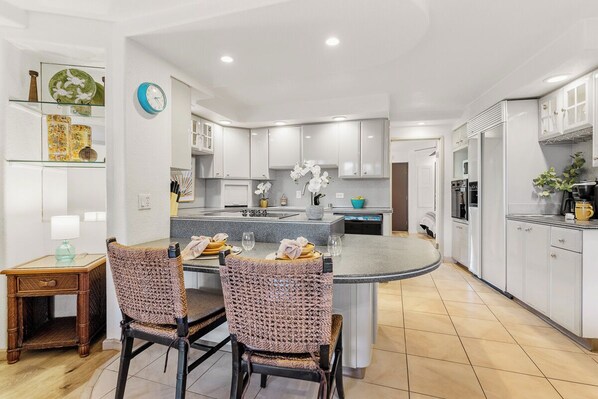 Une cuisine moderne avec des meubles blancs, un îlot central et un coin repas doté de chaises en osier.