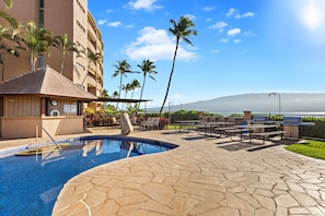 A swimming pool with stone tiles, outdoor seating, palm trees, and a view of the ocean. - Scenic 2BR Retreat Near Maalaea's Pristine Waters (Wailuku)
