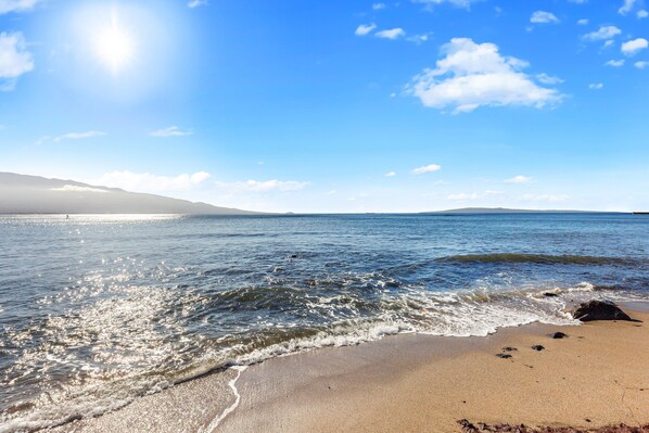 Een strand met heldere lucht, rustig water en verre bergen.