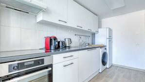 A modern kitchen with white cabinets, a built-in oven, a coffee maker, and a washing machine. - Appartement Alegria - Welkeys (Bandol)
