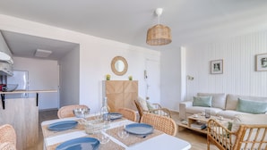 A dining area with a white table set for four, surrounded by wicker chairs. A wicker pendant light hangs above the table. - Appartement Alegria - Welkeys (Bandol)