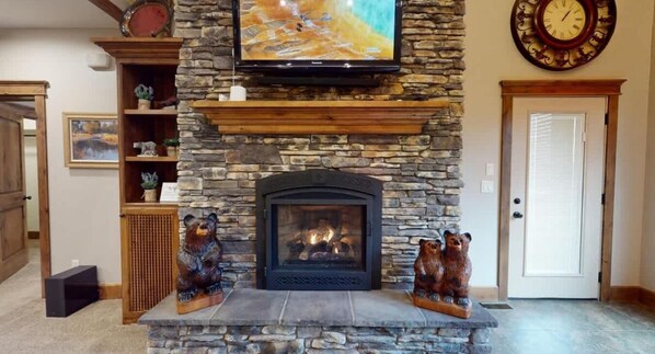 A stone fireplace with two bear sculptures, a mounted television, and a clock on the wall.