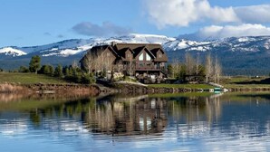 Eine Lodge mit einer großen Holzhütte an einem See, umgeben von schneebedeckten Bergen.