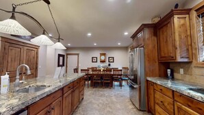 Eine Küche mit Granit-Arbeitsplatten, Holzschränken, einem Edelstahl-Kühlschrank und Pendelleuchten.