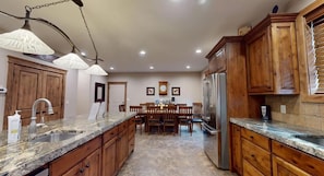 A kitchen with granite countertops, wooden cabinets, a stainless steel refrigerator, and pendant lighting.