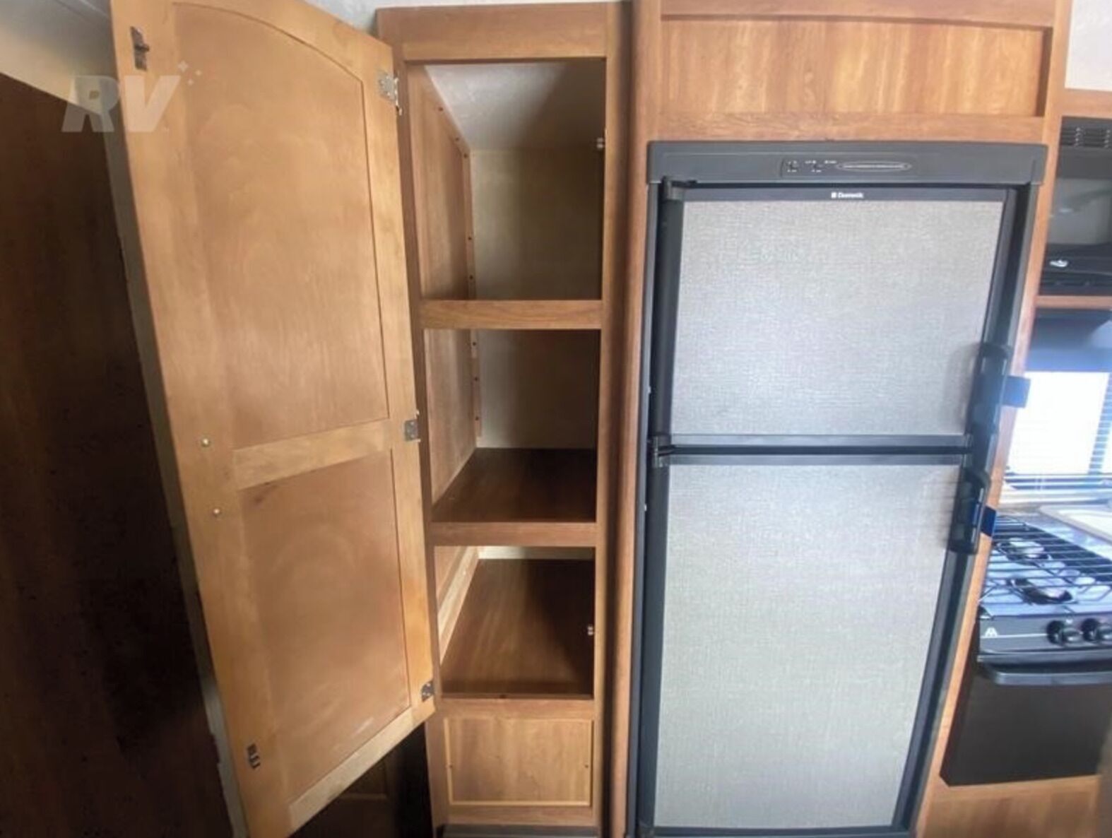 Een kleine keuken met houten kastjes en een zwarte koelkast.