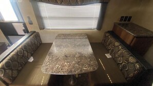 Interior compacto de una caravana, con zona de comedor que incluye una mesa de mármol y asientos acolchados.