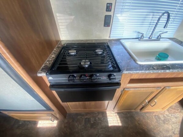 A compact kitchen with a stove, oven, sink, and wooden cabinets.
