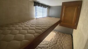 Un dormitorio de caravana compacto con una litera, una ventana con persianas y un armario de madera.