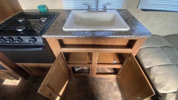 Cocina compacta para autocaravana con estufa a gas, pileta y muebles de madera.