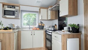 Uma cozinha compacta com micro-ondas, fogão, forno e uma janela com persianas.