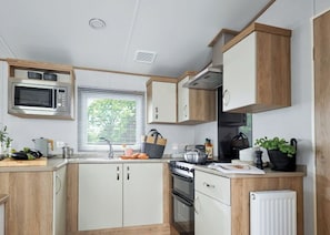 Una cocina compacta con microondas, estufa, horno y una ventana con persianas.