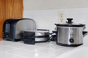 Enjoy cooking in this kitchen with a toaster, slow cooker, and power outlet on a tiled countertop.