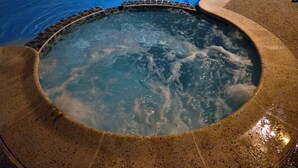 Ein Whirlpool mit gefliestem Rand und ein Pool im Hintergrund.