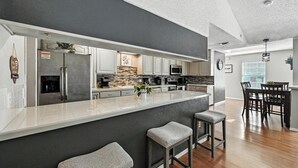 Eine moderne Küche mit einer großen Kochinsel, Edelstahlgeräten und einem Essbereich mit einem dunklen Holztisch und Stühlen.