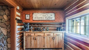 A rustic cabin interior with a wooden bar counter, stone wall, and a sign reading "Coffee Bar". - Log Cabin in the Woods (Munising Township)
