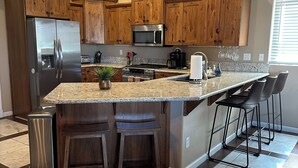A modern kitchen with wooden cabinets, stainless steel appliances, granite countertops, and a bar area with stools.
