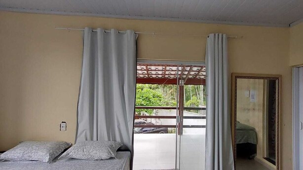 A room with a bed, a sliding glass door leading to an outdoor area, and a mirror on the wall. - Quarto Para Grupo até 4 Pessoas Praia da Maranduba Ubatuba Sp (Sertão da Quina Ubatuba)