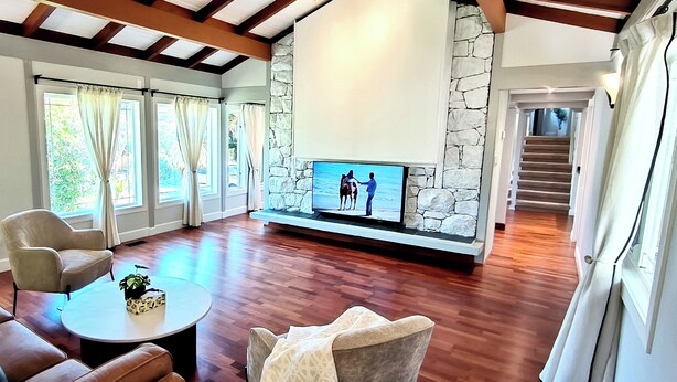 A spacious living room with a stone accent wall, a flat-screen TV, and a wooden staircase.