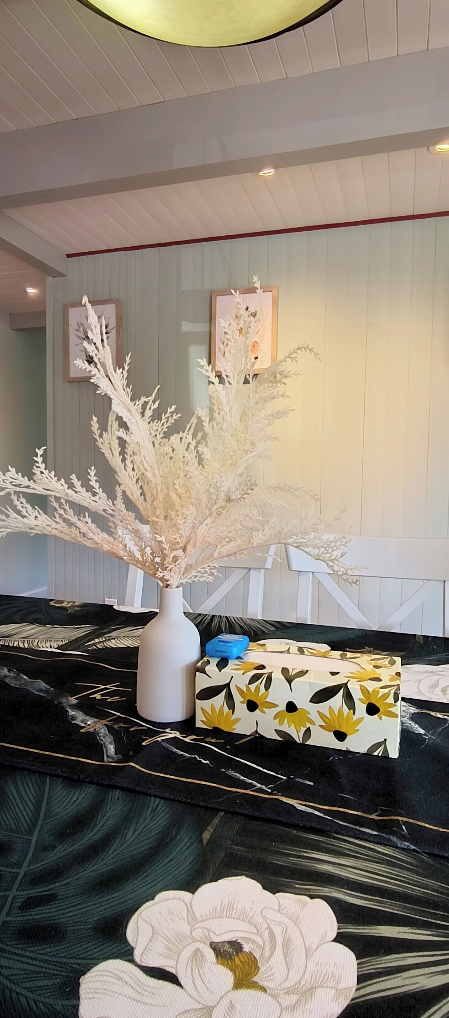 Un salon moderne avec un vase blanc, une boîte à motifs et une grande fleur posée sur un canapé noir et blanc à motifs.