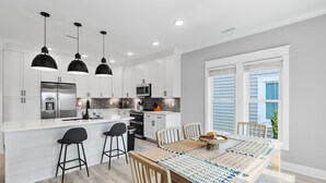 Una cocina moderna con armarios blancos, electrodomésticos de acero inoxidable e iluminación colgante negra.