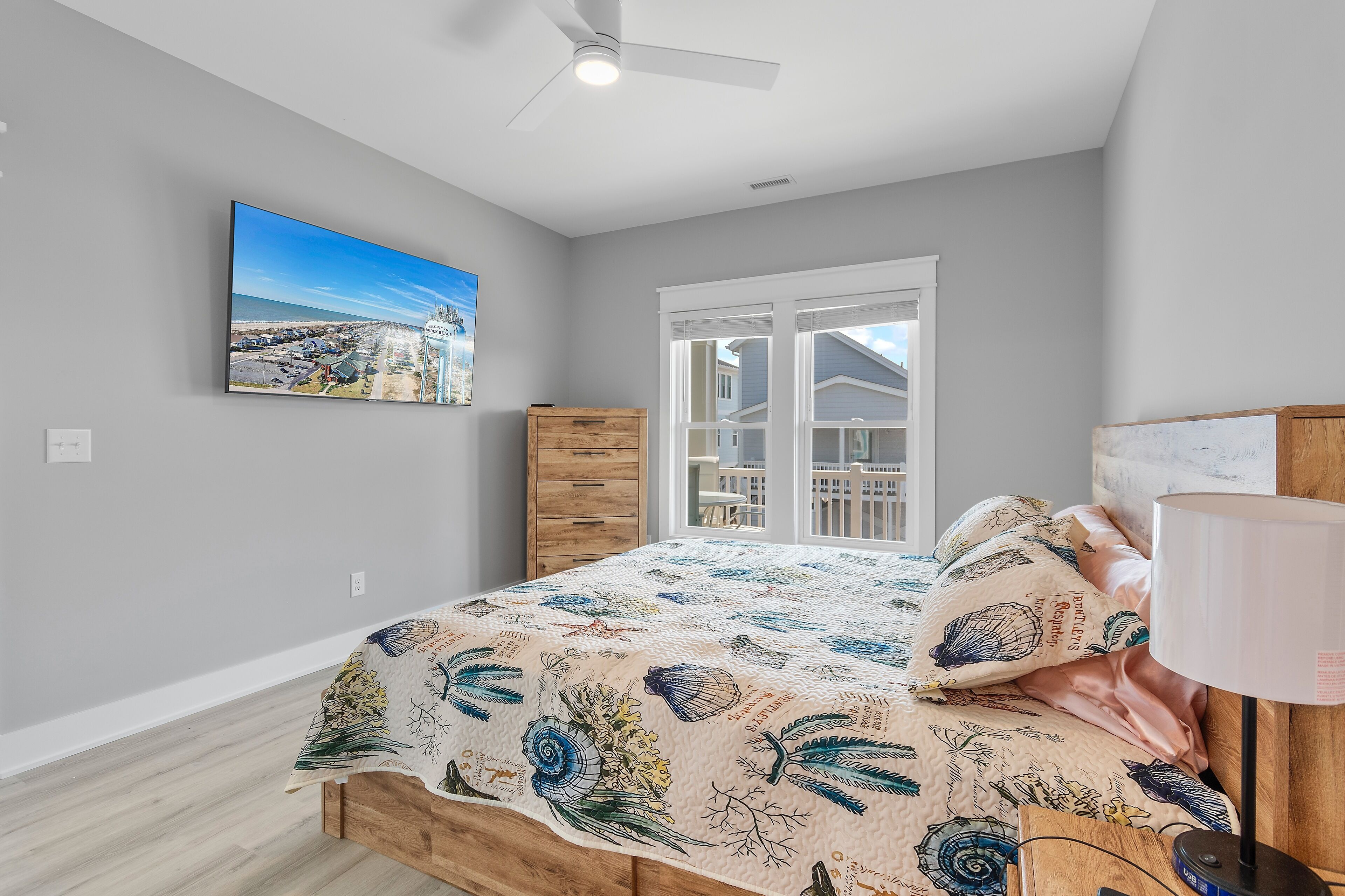 A bedroom with a bed, a nightstand, a lamp, a dresser, and a window with a view of houses.