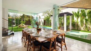 A modern dining area with a glass wall, a pool, and a well-maintained garden.